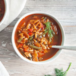 overhead view of vegan orzo soup in a white soup bowl with a spoon