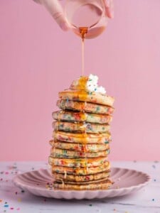 Pouring maple syrup on tall stack of Funfetti Pancakes