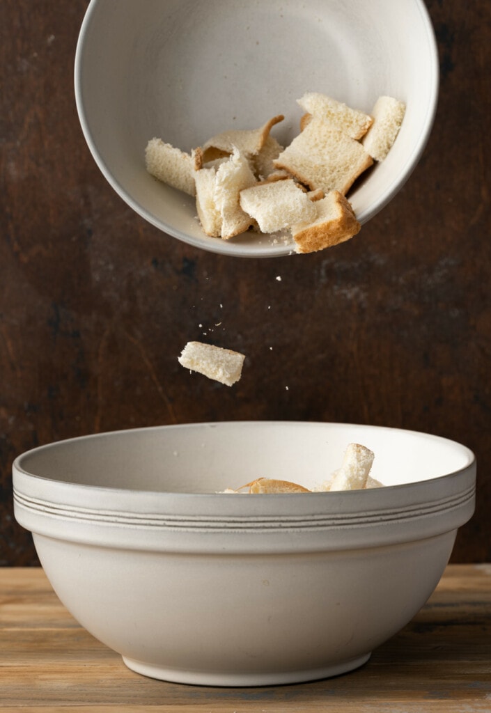 Adding cubed stale bread to a large mixing bowl to make bread pudding