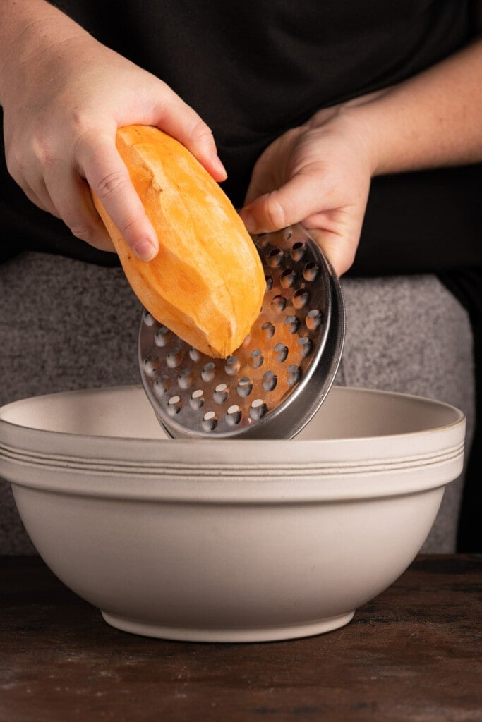 Using a cheese grater to shred sweet potato