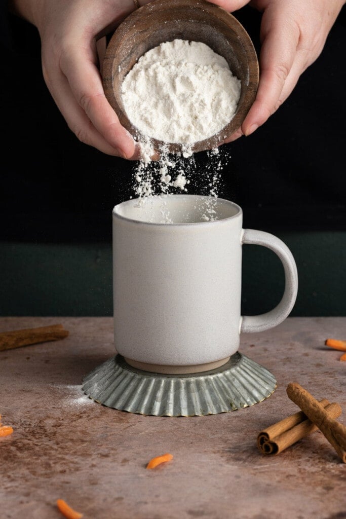 Adding flour to a mug to make a carrot mug cake