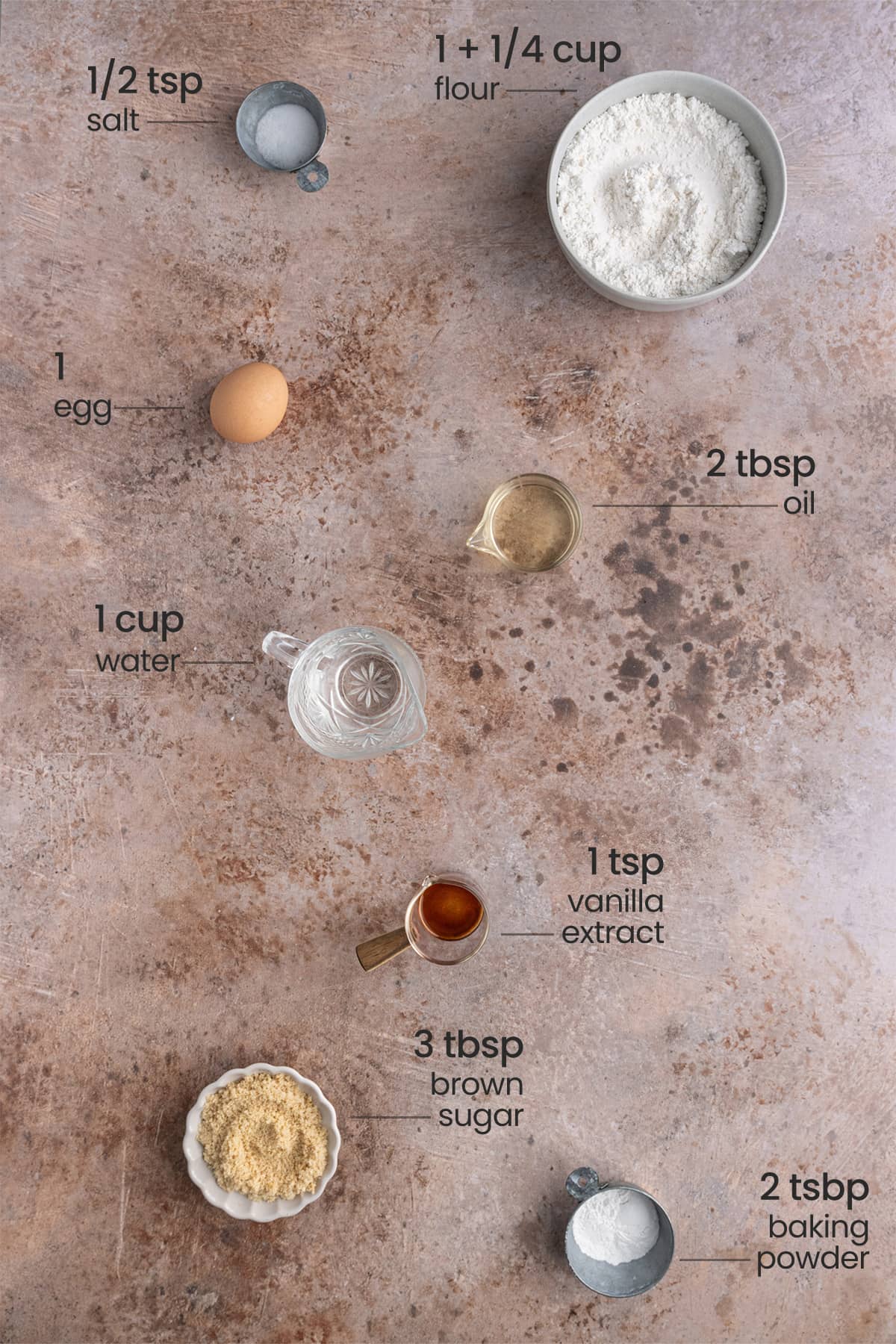 Overhead view of the ingredients for Dairy-Free Waffles - salt, flour, egg, oil, water, vanilla extract, brown sugar, and baking powder.
