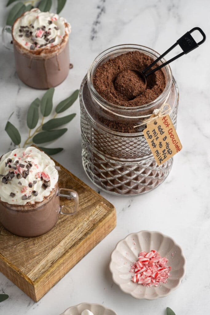 Hot Chocolate Mix surrounded by two mugs of hot chocolate