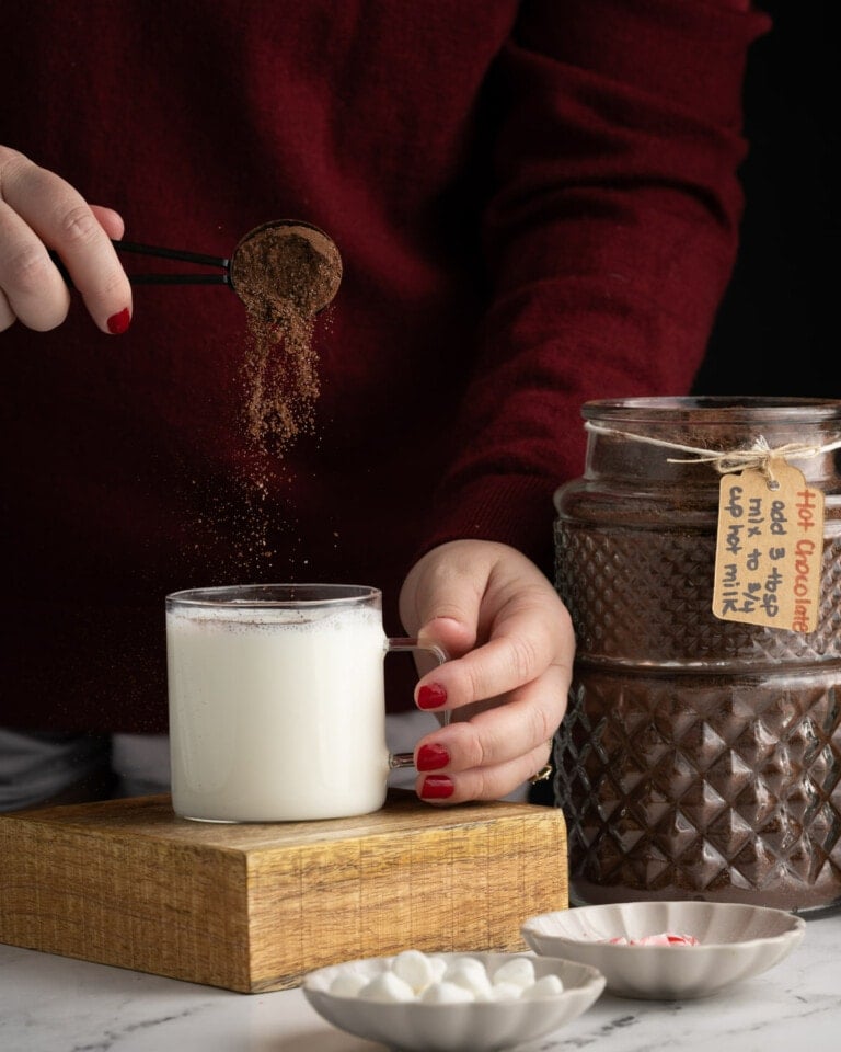 Adding hot chocolate mix with chocolate chips to a mug with hot milk