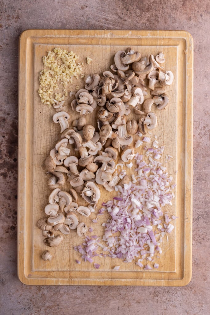Prepped garlic, mushrooms, and shallots on a cutting board