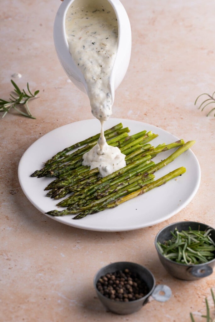 Pouring Shallot Cream Sauce over roasted asparagus