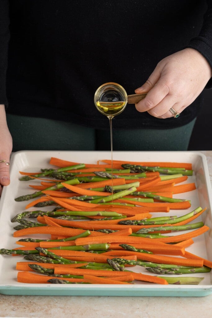 Adding olive oil to carrots and asparagus to roast