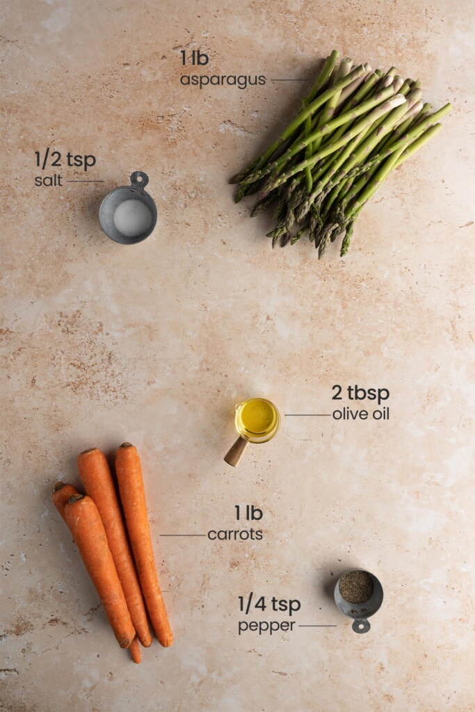 overhead view of asparagus, salt, olive oil, carrots and black pepper on a tan marbled background