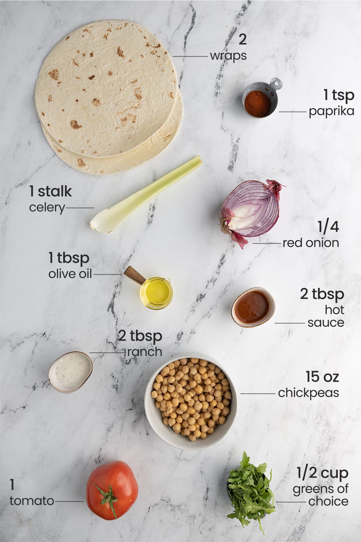 overhead view of all ingredients for buffalo chickpea wrap - wraos, paprika, celery, red onion, olive oil, hot sauce, ranch, chickpeas, tomato, greens