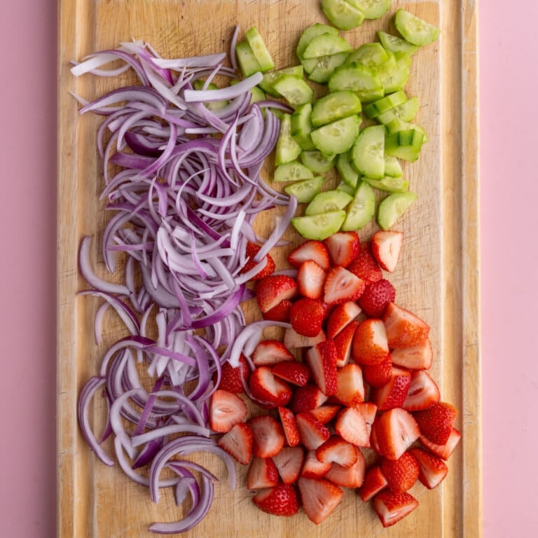 Prepping red onion, cucumber, and strawberries for salad