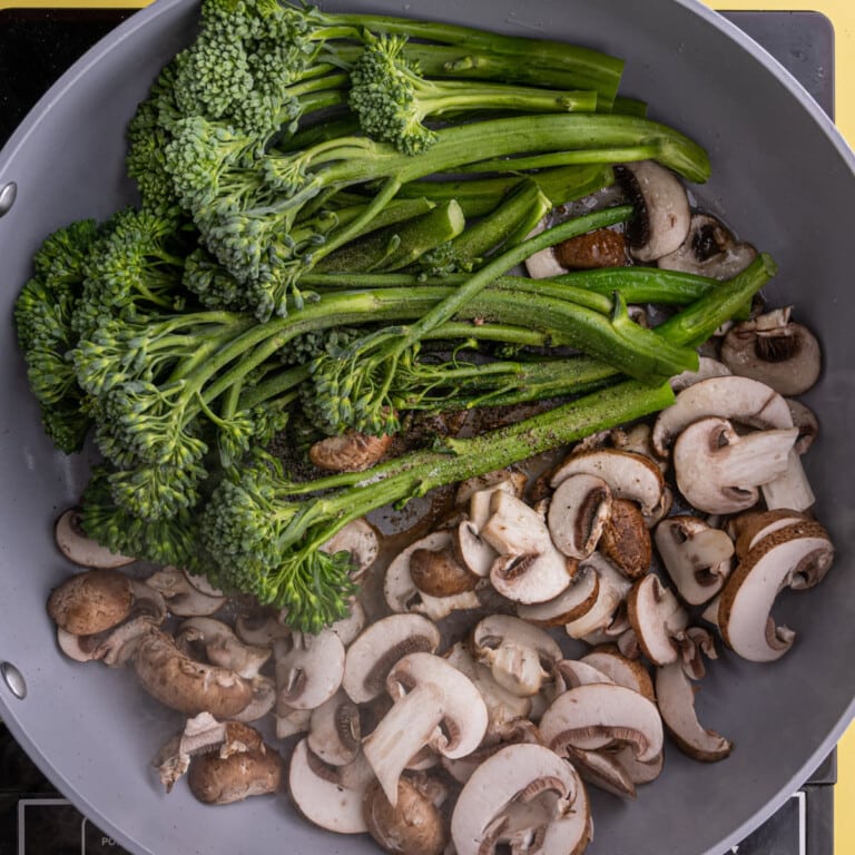 Adding mushrooms and broccolini to a pan with hot oil