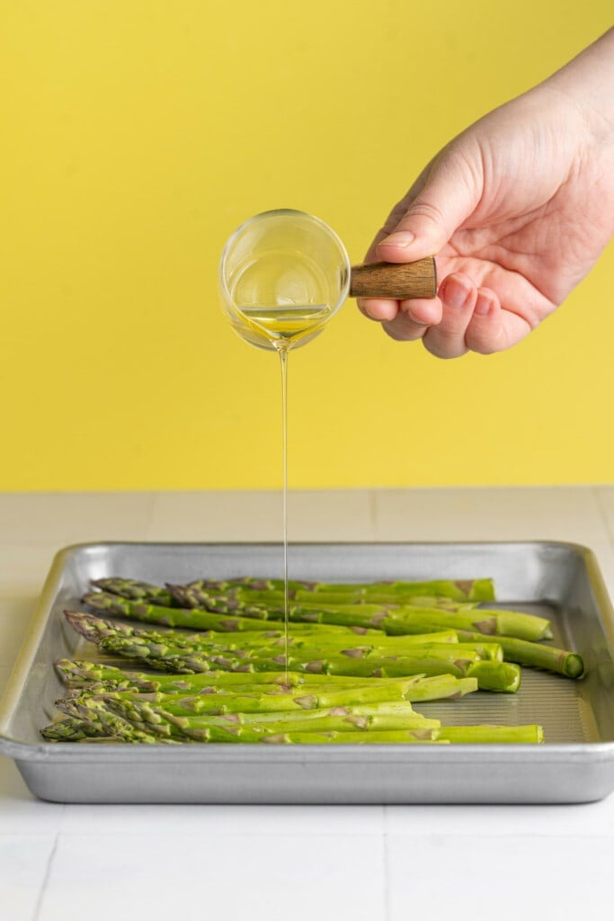 Adding olive oil to asparagus and garlic to roast