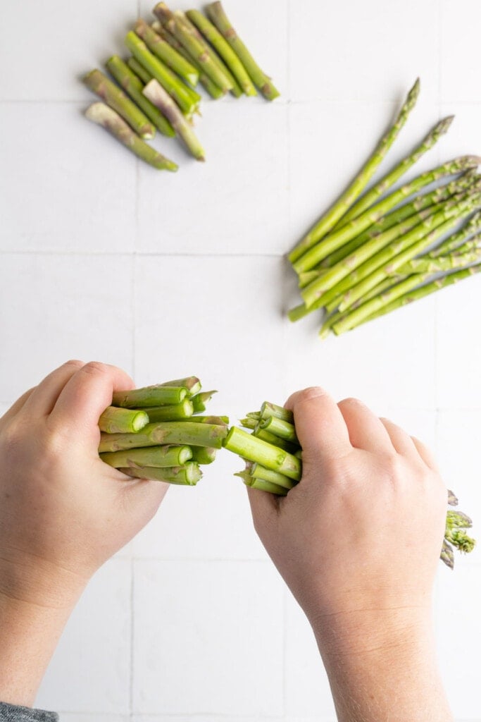 Snapping woody ends off asparagus with already prepped asparagus in the background