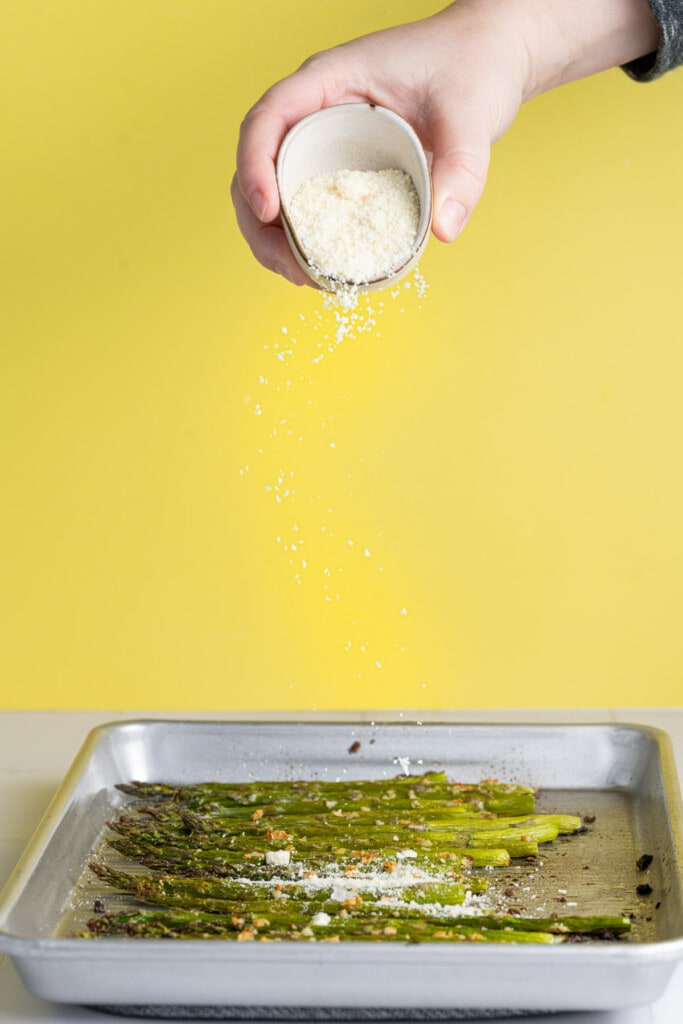 Sprinkling Parmesan cheese on roasted garlic and asparagus