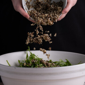 Mixing together quinoa and arugula together to make the base of a salad