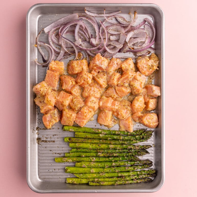 Onion, salmon, and asparagus on a baking sheet ready to roast