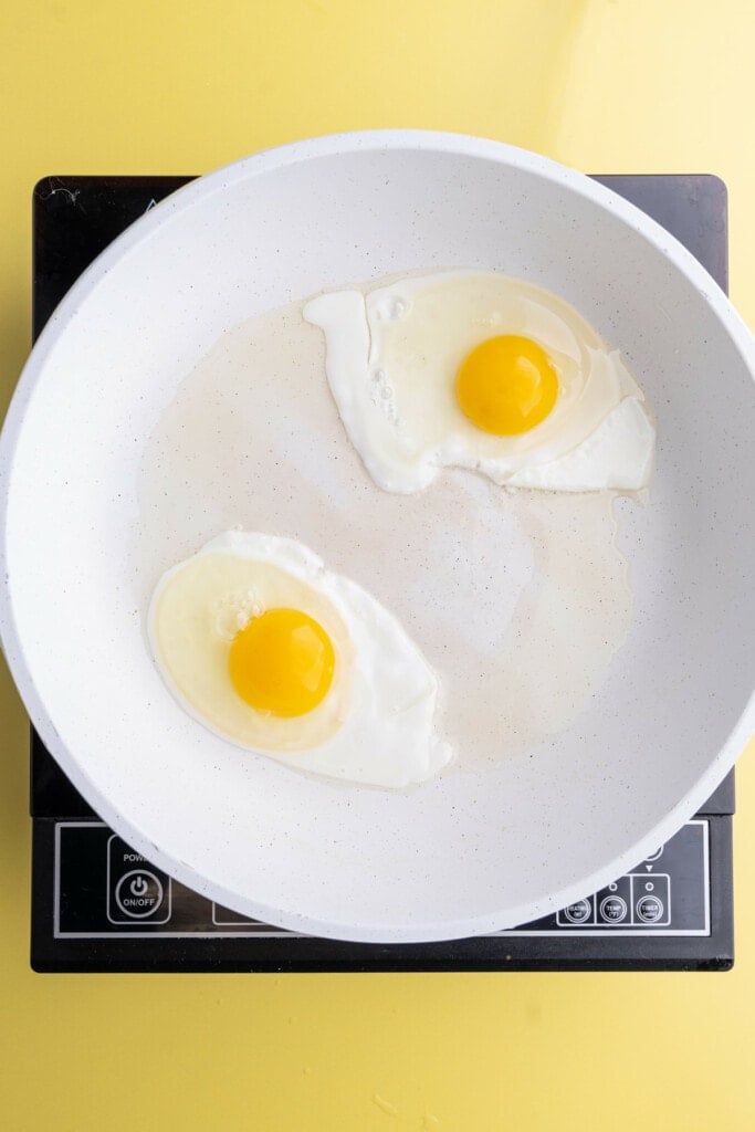 Frying two eggs in a white pan