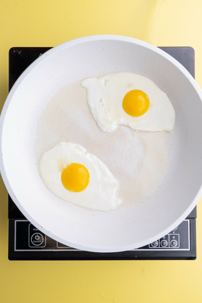 Two eggs frying in a pan with opaque egg whites