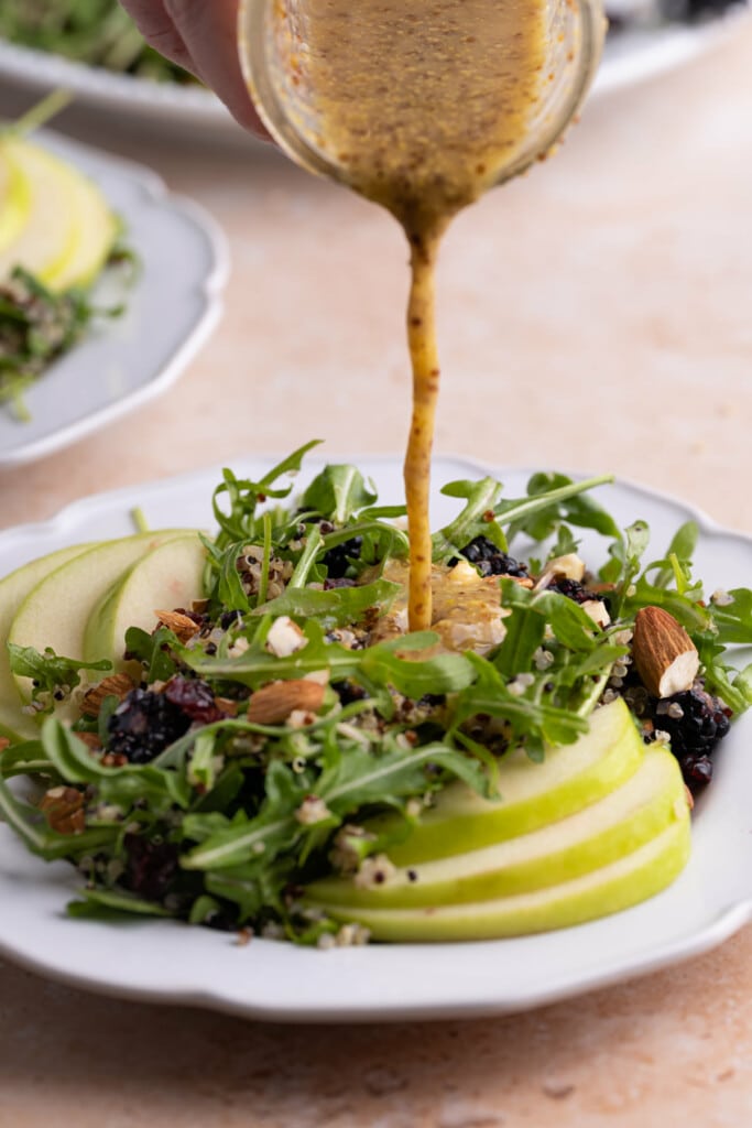 Pouring honey Dijon vinaigrette over Arugula Quinoa Salad