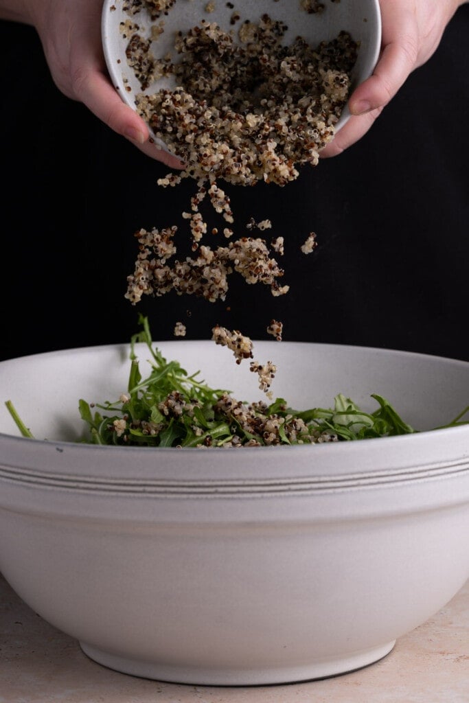 Tossing arugula and quinoa together for the base of a salad