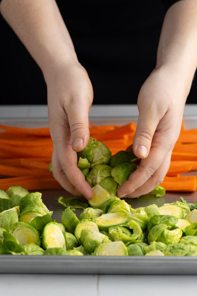 Using clean hands to toss carrots and brussels sprouts in olive oil