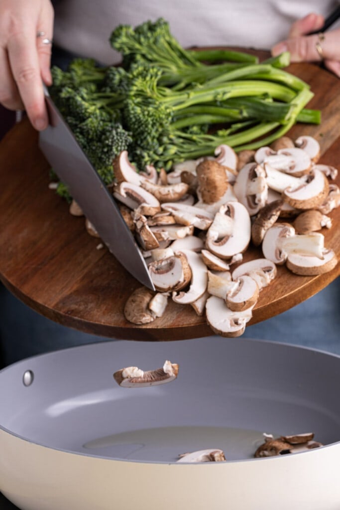 Adding broccolini and mushrooms into a frying pan