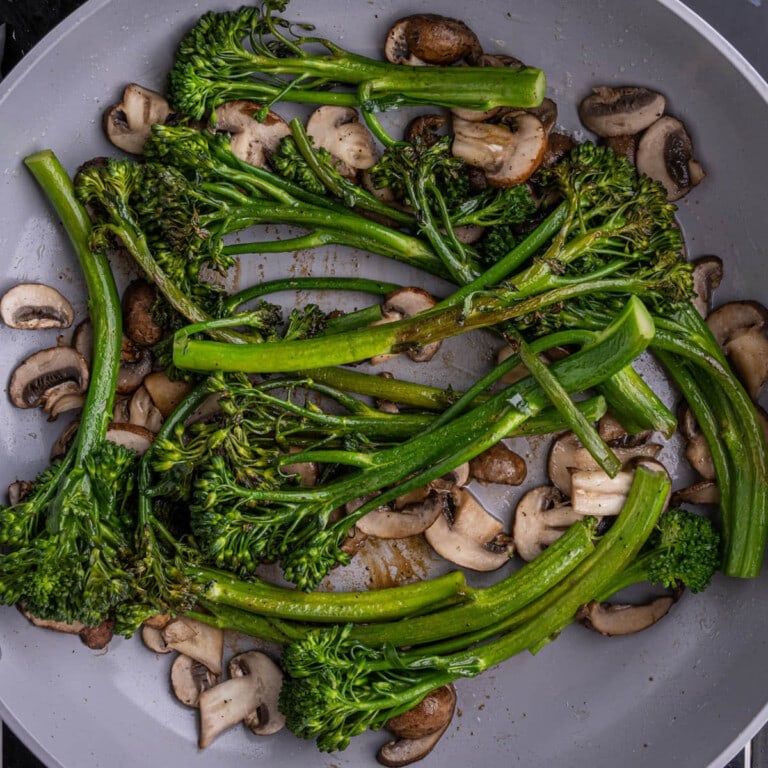 Browned broccolini sitting atop mushrooms in a pan