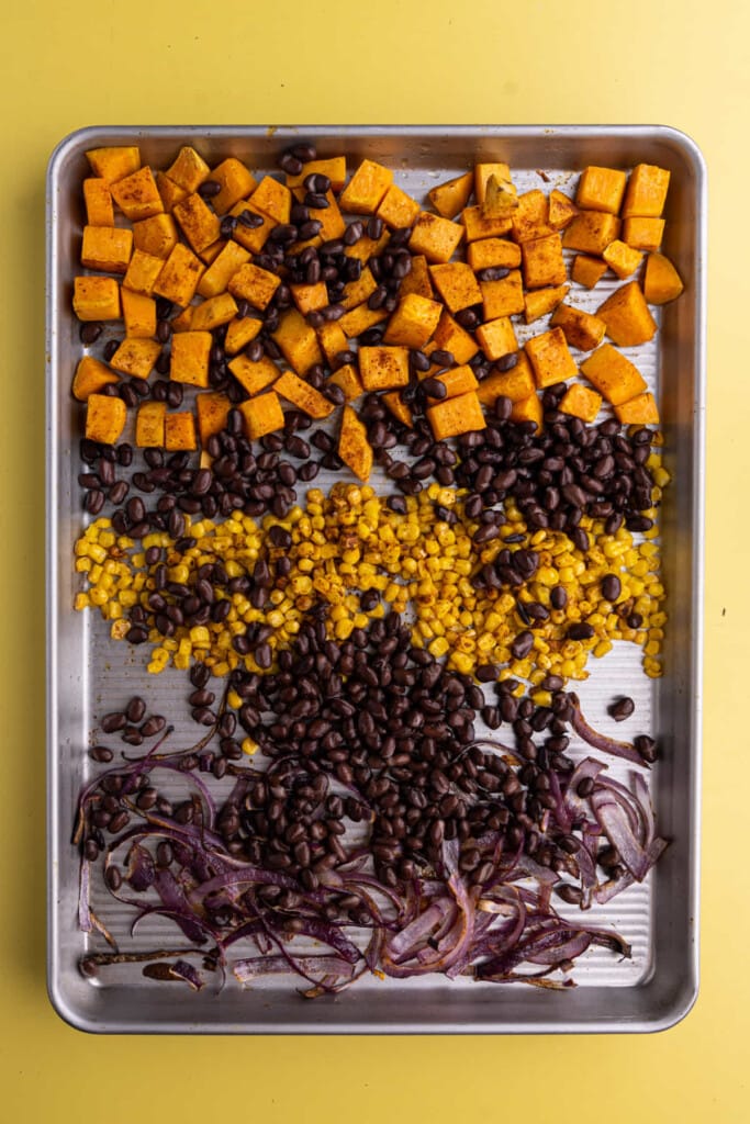 Adding black beans to baking sheet with roasted vegetables