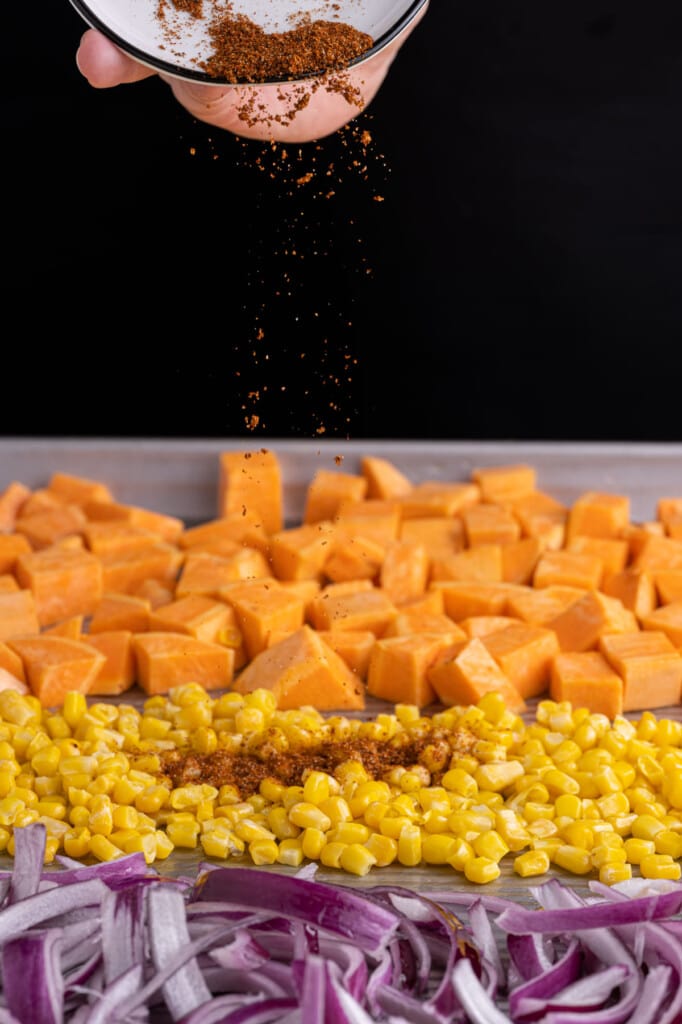 Adding taco seasoning to sweet potatoes, corn, and red onion to roast