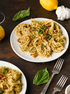 Tahini pasta with toasted walnuts plated on a table with a lemon for zest and wine glasses