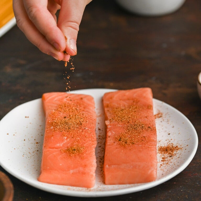 Sprinkling cajun seasoning over salmon