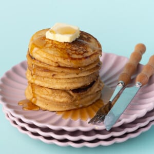 Stack of brown sugar pancakes with dripping syrup on pink plates