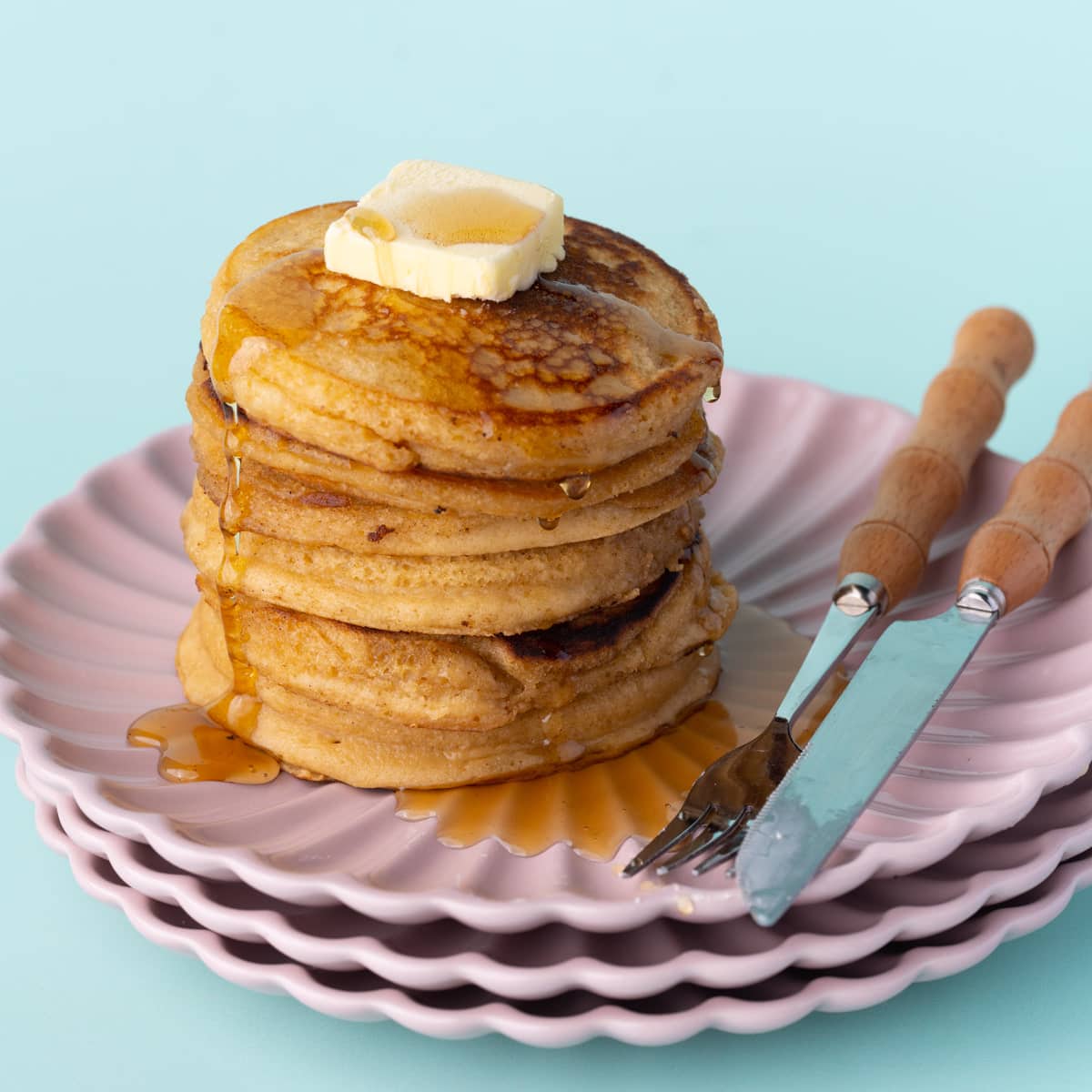 Stack of brown sugar pancakes with dripping syrup on pink plates