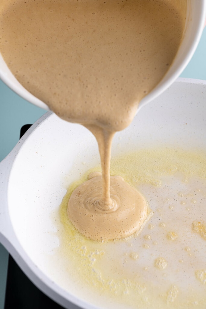 Pouring brown sugar pancake batter into pan with melted butter