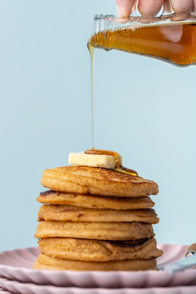 Pouring syrup over stack of pancakes with brown sugar