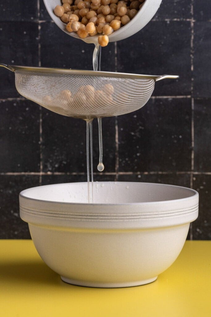 Running chickpeas through a sieve to strain aquafaba