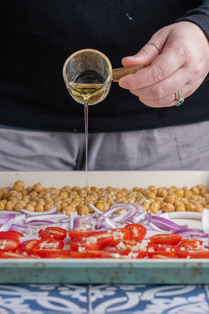 Coating prepped chickpeas, red onion, and grape tomatoes in olive oil, salt and pepper