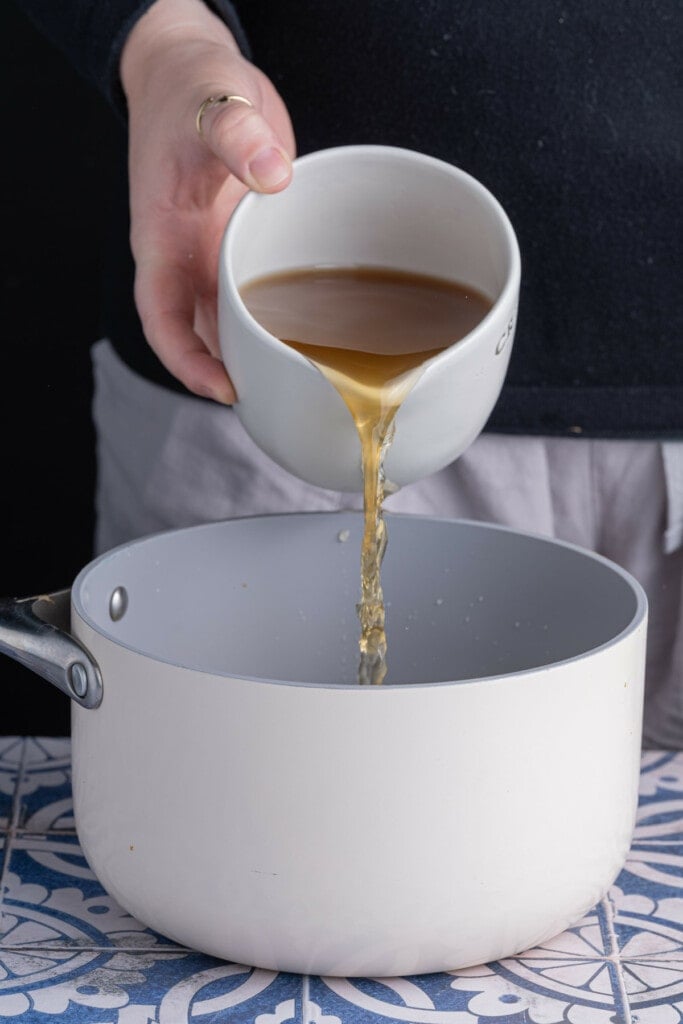 Adding vegetable broth to a pot to cook quinoa in