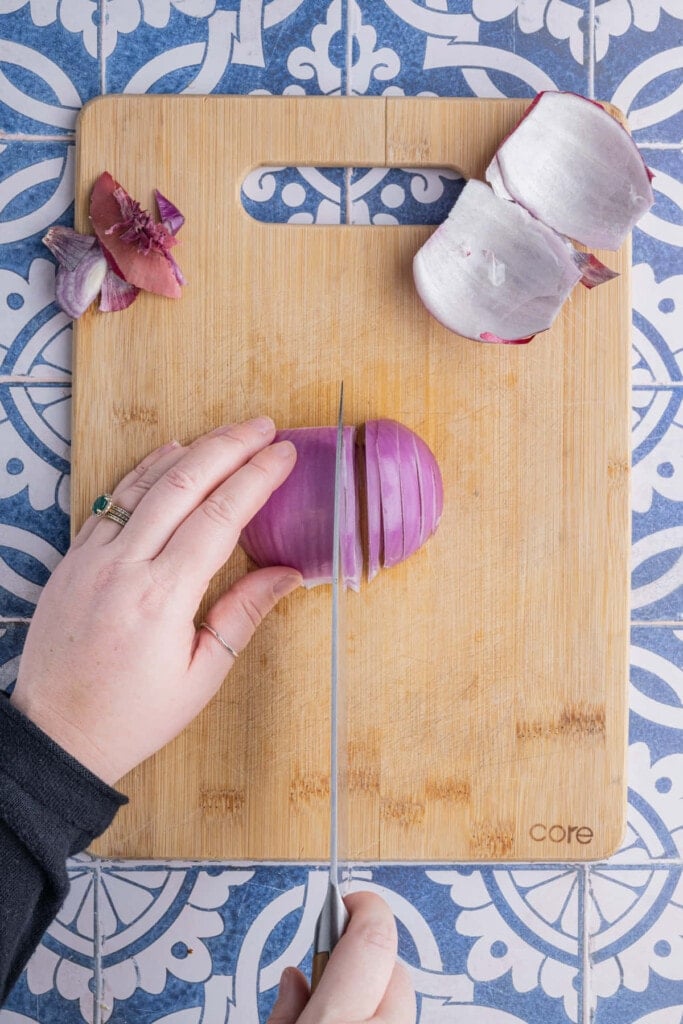 Laying a prepped red onion half flat on a cutting board to slice it thin