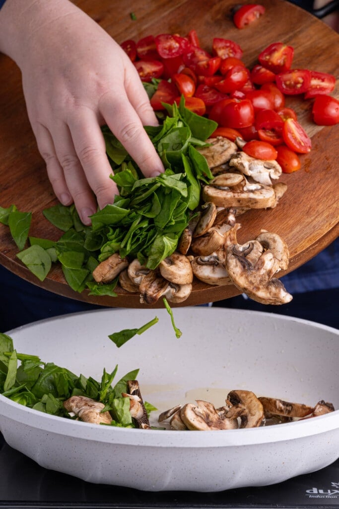 Adding vegetables to pan to fry for breakfast bowl