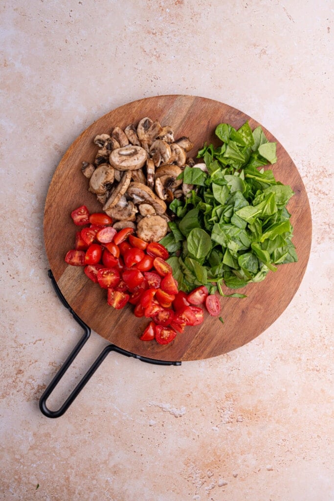 Prepped grape tomatoes, spinach, and mushrooms ready to fry in a pan