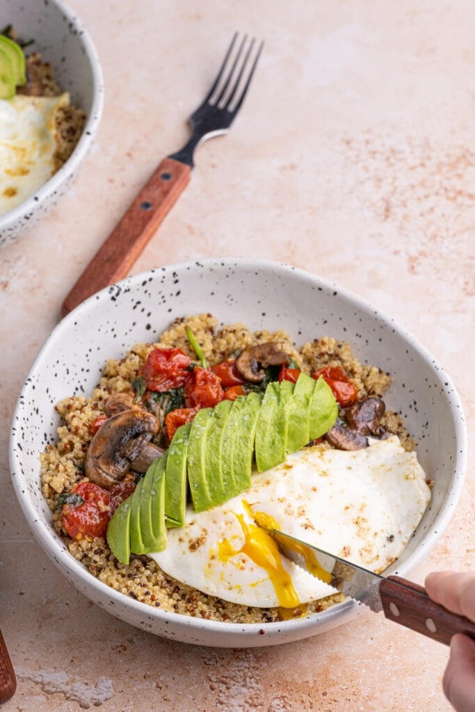 Cutting into runny egg yolk on breakfast bowl