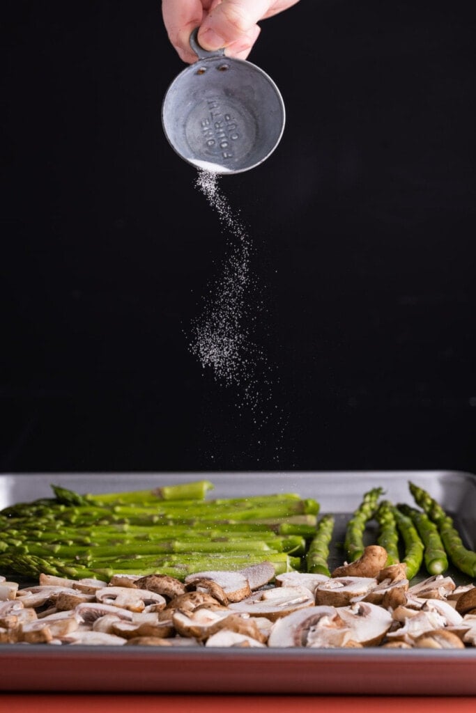 Adding salt to asparagus and mushrooms on a baking sheet