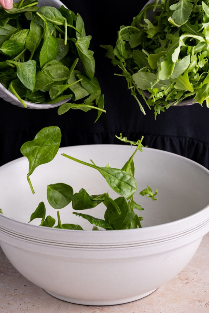 Adding spinach and arugula together in a large mixing bowl