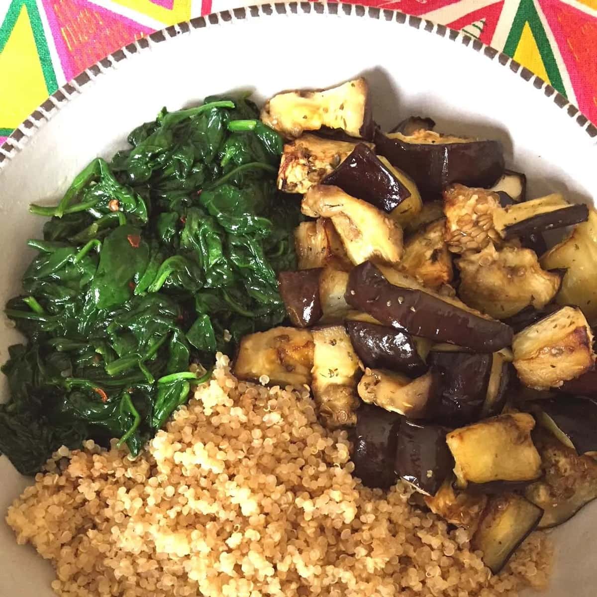 Close up of a spinach eggplant quinoa bowl on a colorful table