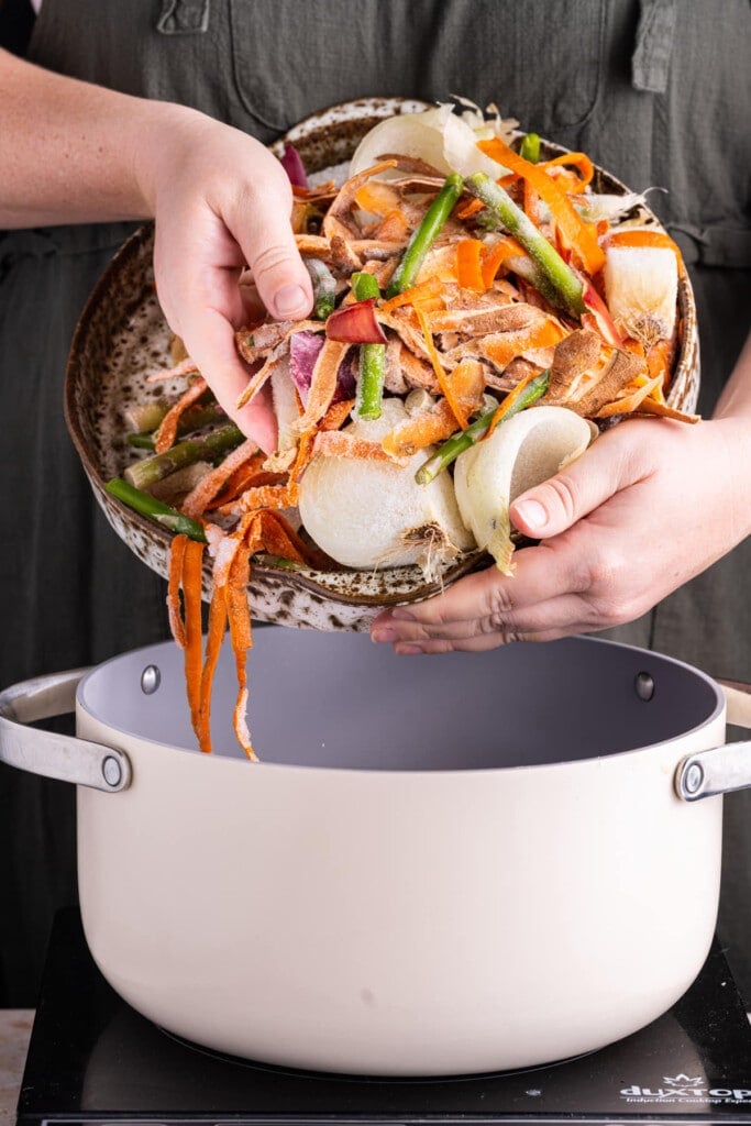 Adding veggie scraps to a large pot to make vegetable broth