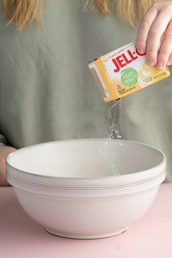 Adding instant jello mix to a mixing bowl to make a custard