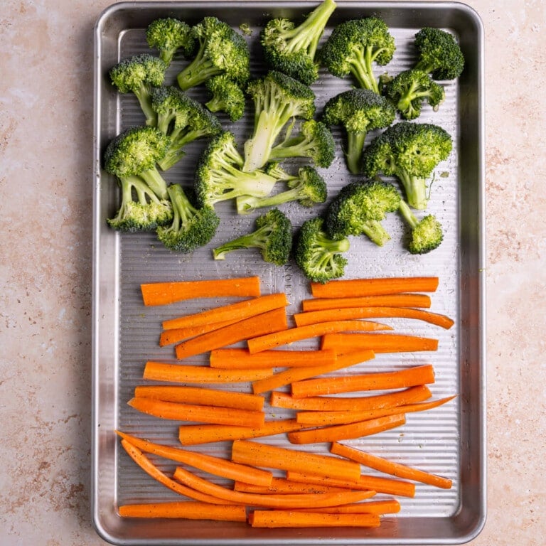 Broccoli and carrots coated in olive oil, salt, and pepper ready to roast in the oven