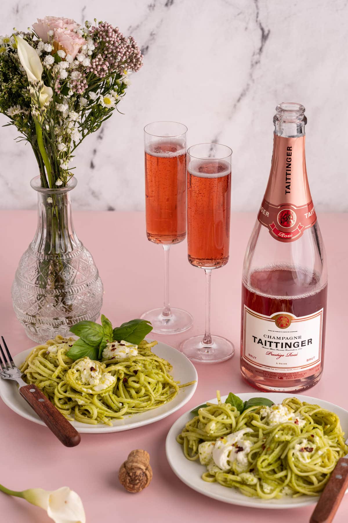 Tablescape with two portions of Burrata Pesto Pasta, two glasses of rose, and flowers
