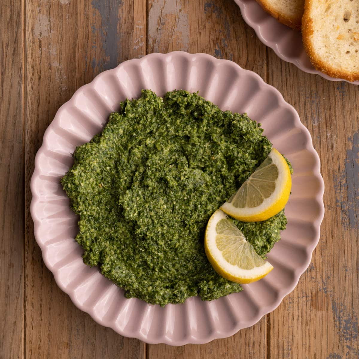 Carrot Top Pesto on a pink plate with two lemon wedges